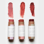 Three Among The Flowers Cheek + Lip  sticks with swatches of color on a white background