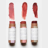 Three Among The Flowers Cheek + Lip  sticks with swatches of color on a white background