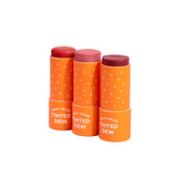Three orange sticks of Axiology Multi-Stick Tinted Dew' on a white background