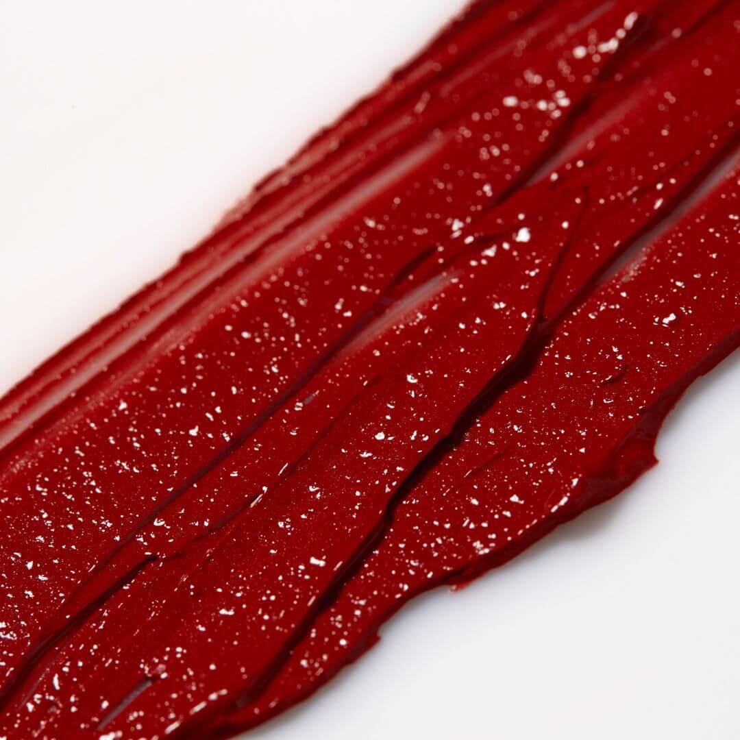 Close-up of red Axiology 'Strength"  lipstick swatch on a white background