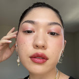 Close-up of a person with, wearing earrings and a necklace and Axiology Clarity Makeup stick