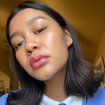 Close-up of a woman wearing axiology multi-stick in shade joy with dark hair and pink lipstick indoors.