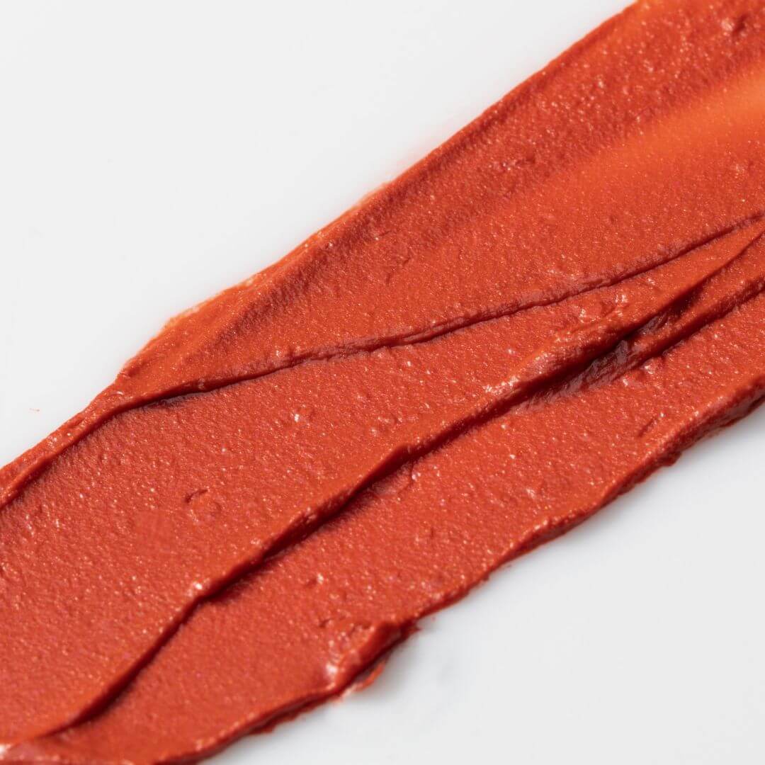 Close-up of a swatch of Axiology Tinted Dew Radiance red lipstick on a white background