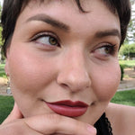 Close-up of a woman with short hair and green eyes, wearing Axiology Lipstick in shade True