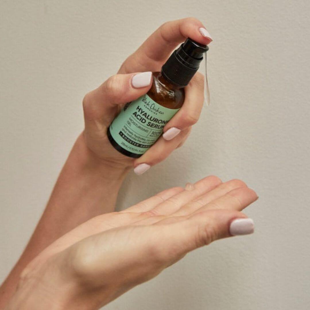 Hand holding a bottle of Black Chicken hyaluronic acid serum against a neutral background