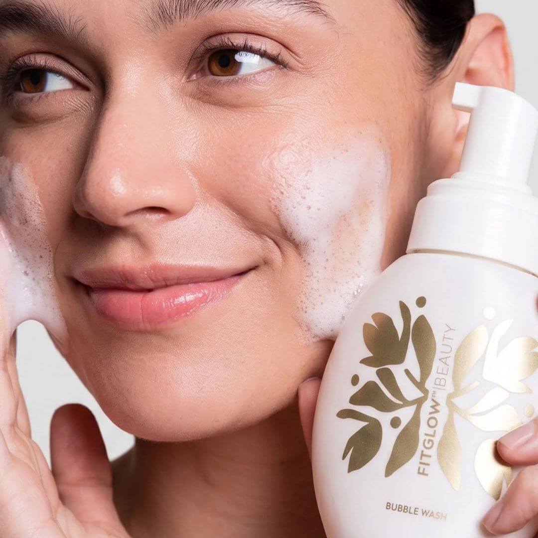 A close-up of a woman applying or washing her face with Fitglow Bubble Wash
