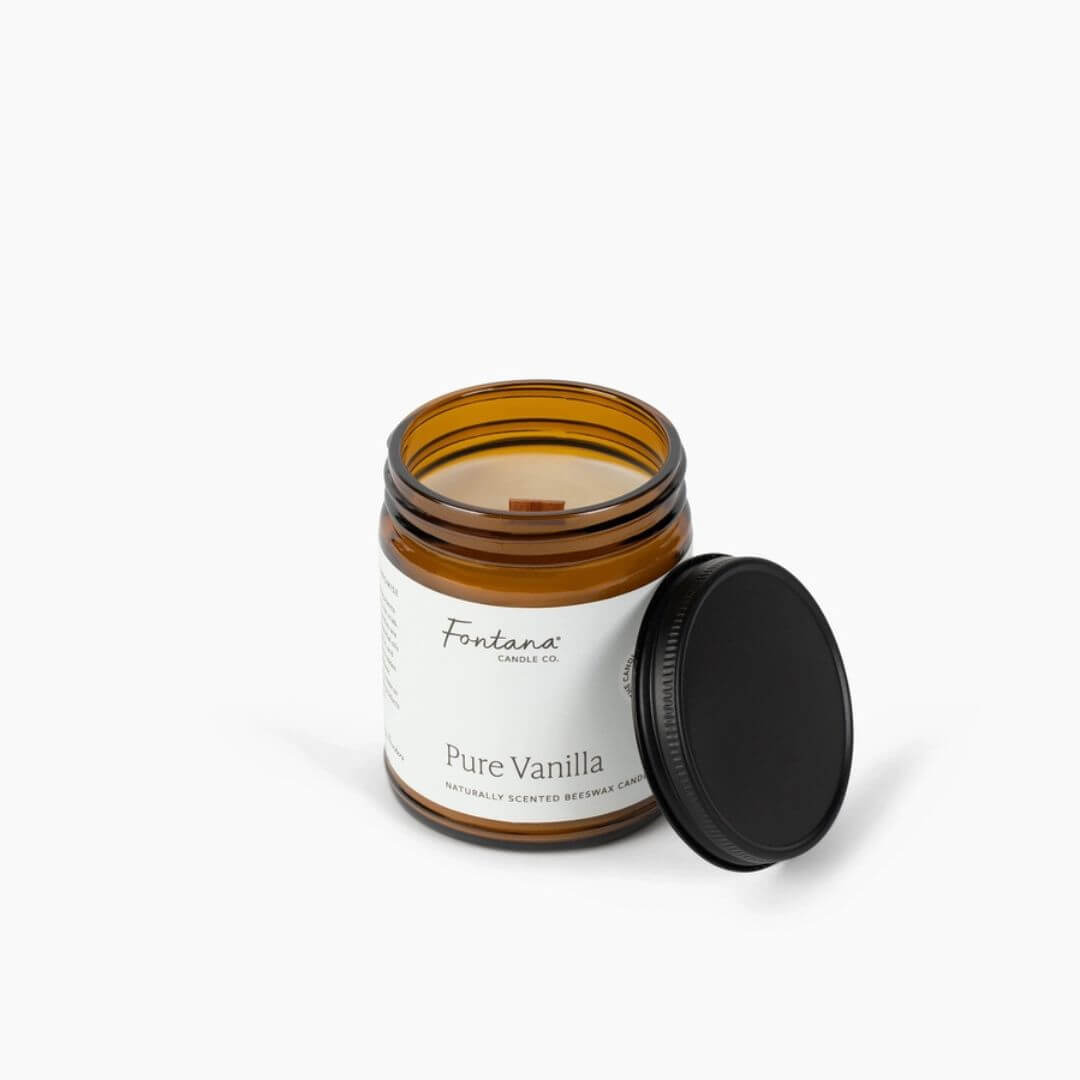 An amber glass jar candle with a white label reading 'Fontana Candle Co. Pure Vanilla' and its black lid resting beside it on a clean white background.
