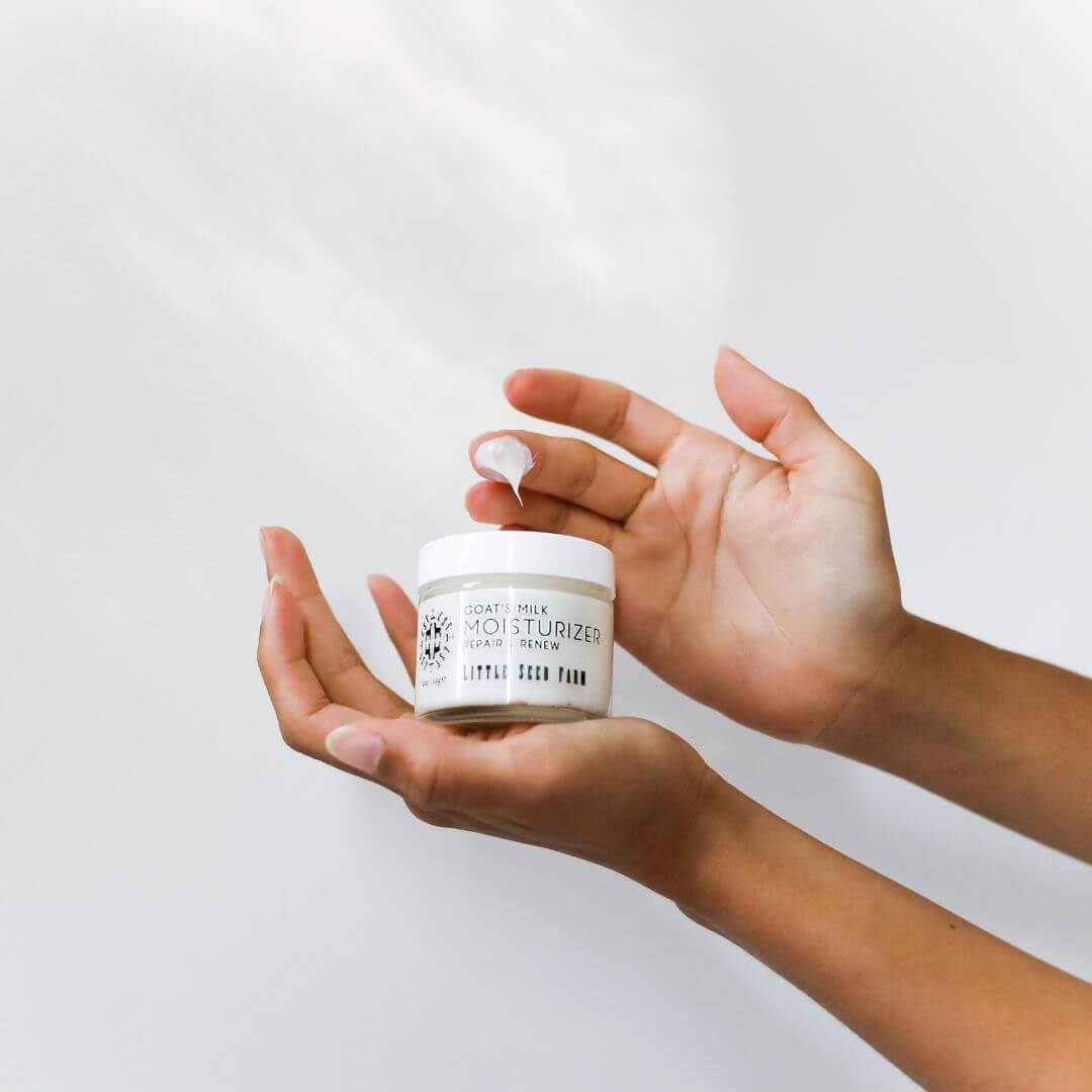 Person holding a jar of Little Seed Farm goat milk moisturizer with a white background
