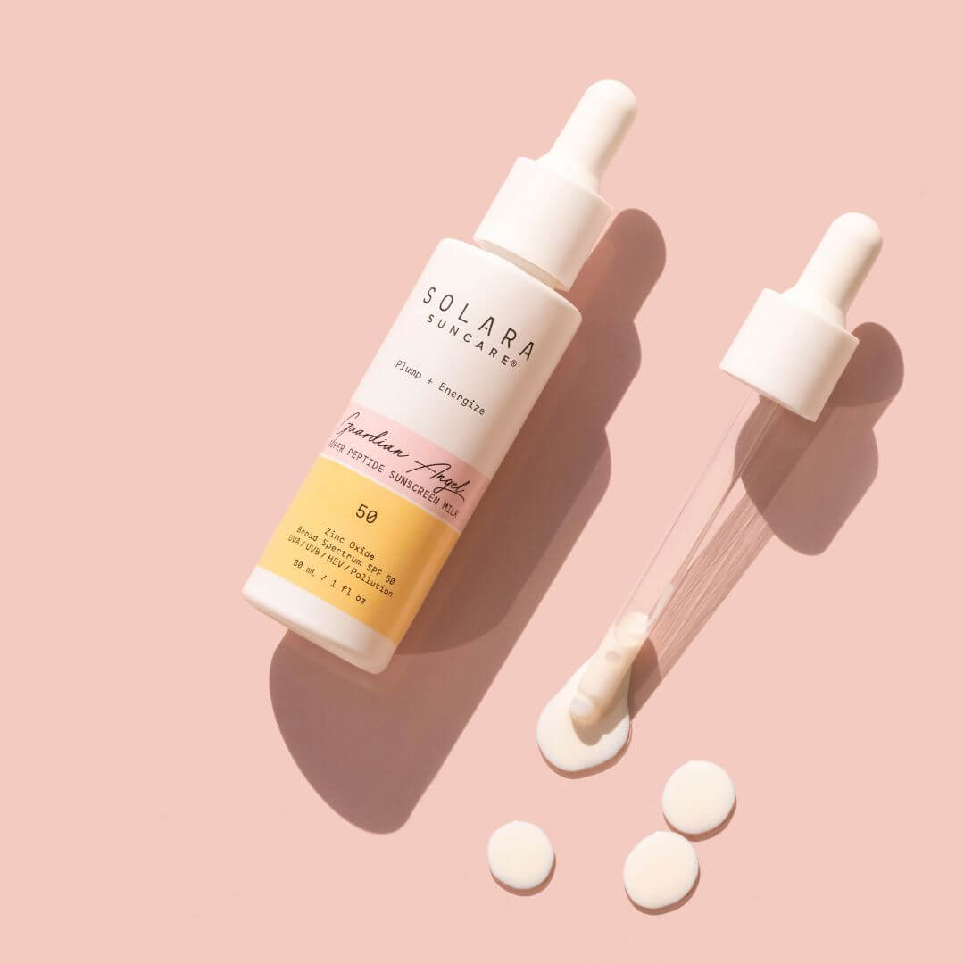 A bottle of Solara Skincare 'Guardian Angel' moisturizing sunscreen with a dropper, shown next to a clear dropper tube and three white circular pills on a solid pink background.