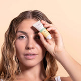 Woman holding tube of solara day dreamer peptide eye cream to her face with a beige background