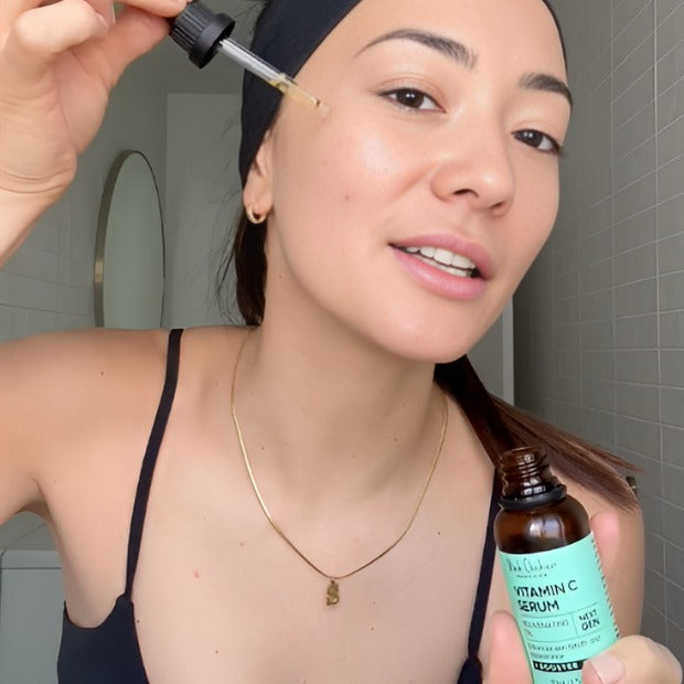 Woman applying vitamin C serum to her face in a bathroom setting