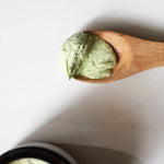 Wooden spoon with green Among the Flowers Calming Baby cream on a white background