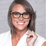 Woman with gray hair wearing glasses and a white shirt against a gray background