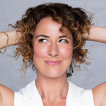 Woman with curly hair touching her hair against a gray background