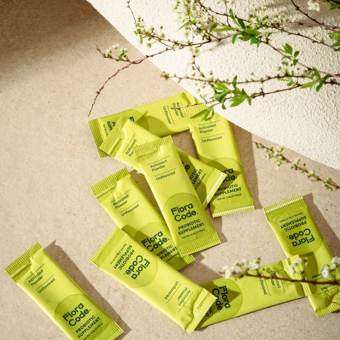 Green packets of Flora Code supplement on a beige surface with floral elements.