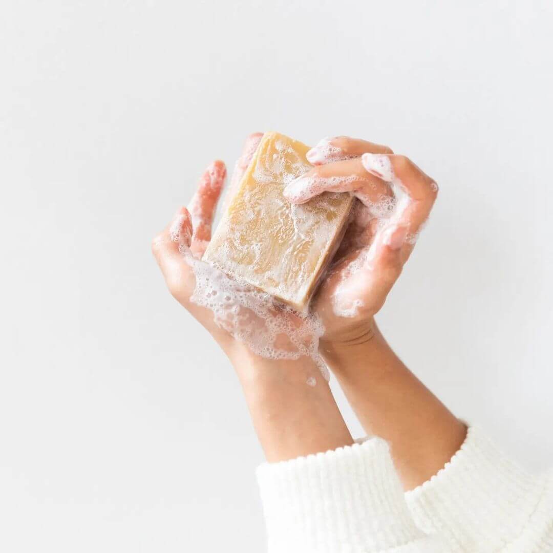 Hands holding a bar of Holiday Soap with lather on a light background