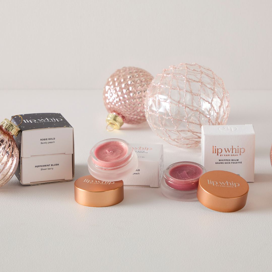 Lip whip lip balm containers and packaging on a white surface with decorative spheres.