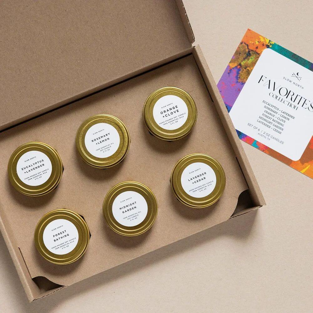 Set of small candles with gold lids in a cardboard box, with a card on the side. slow north