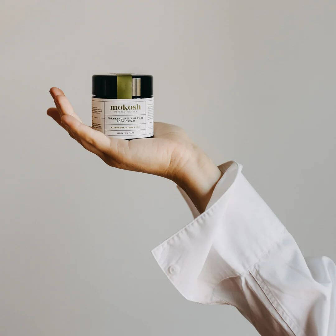 Hand holding a jar of mokosh skincare product against a plain background