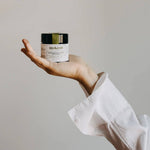 Hand holding a jar of mokosh skincare product against a plain background