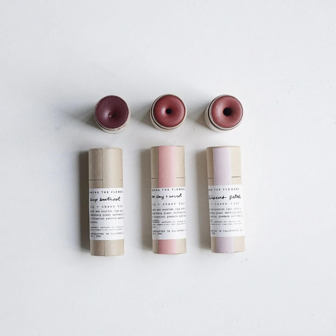 Three lip + cheek tint  tubes from Among the Flowers with pink tops on a light gray background