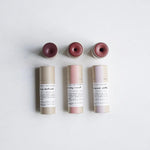 Three lip + cheek tint  tubes from Among the Flowers with pink tops on a light gray background