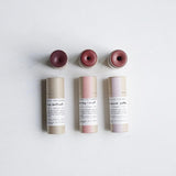 Three lip + cheek tint  tubes from Among the Flowers with pink tops on a light gray background
