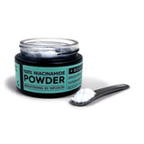 Jar of niacinamide powder with a spoonful on a white background