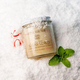 A jar of Little Seed Farm Holiday Sugar Scrub, scented with peppermint and vanilla, styled on a bed of white sugar with mint leaves and candy canes.