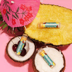 Crazy Rumors Pina Colada lip balm on a pineapple, coconut, and cherry with a pink umbrella on a pink background.