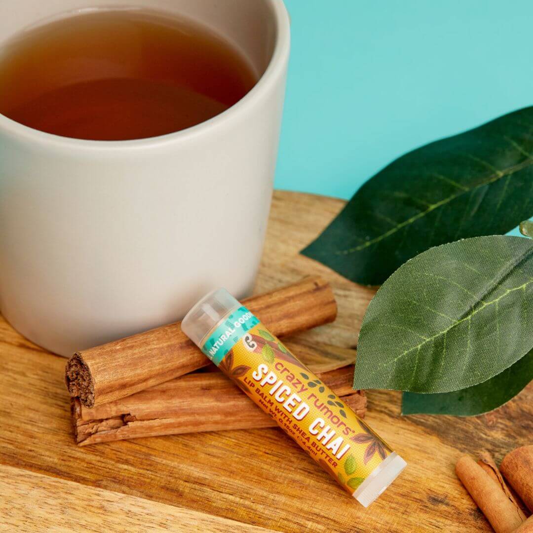 Spiced Chai flavor lip balm with a cup of tea, cinnamon sticks, and leaves on a wooden surface.