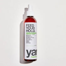 Bottle of 'Feed Your Hold' hair spray with a white label on a light gray background